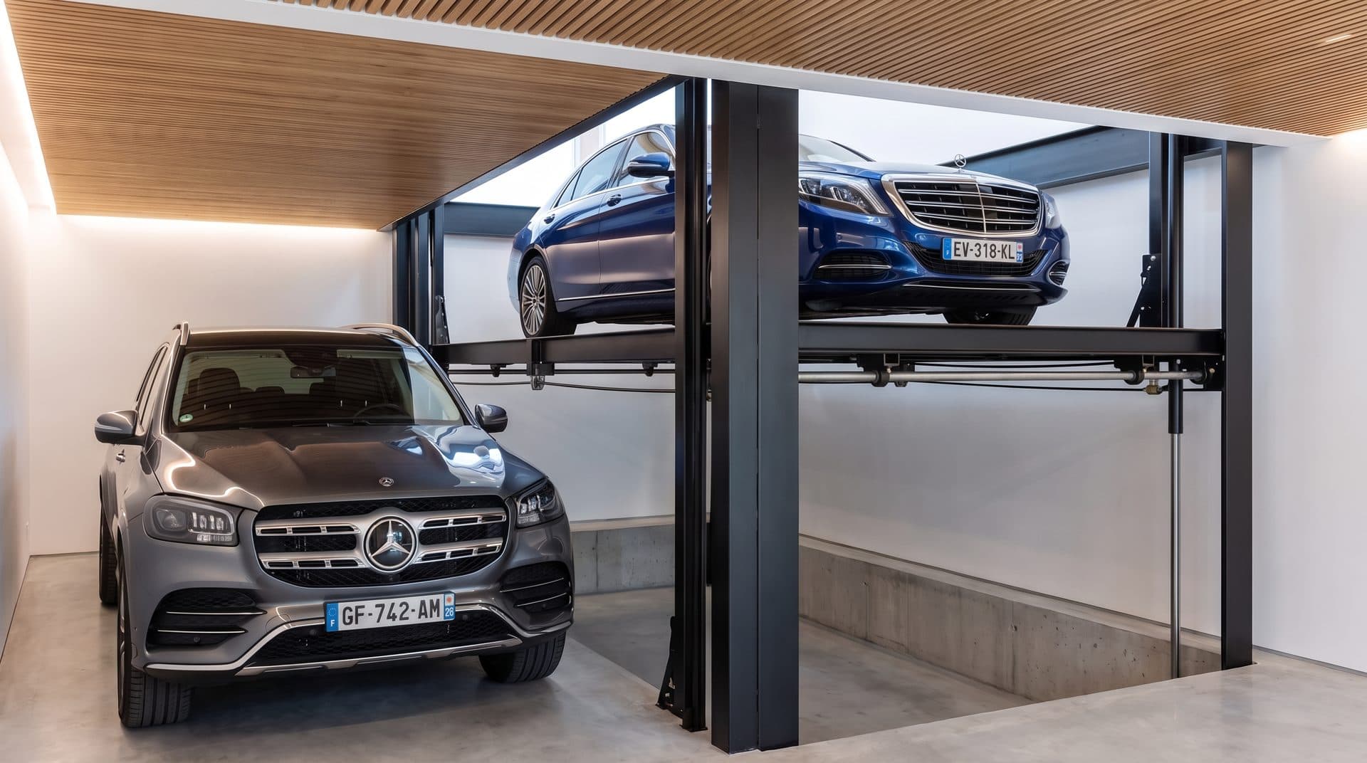 Garage de villa : berline sur la plateforme levée d'un monte-voiture au-dessus de sa fosse en béton, SUV garé à côté